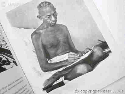 Mahatma Gandhi sitting on the floor and writing a letter.